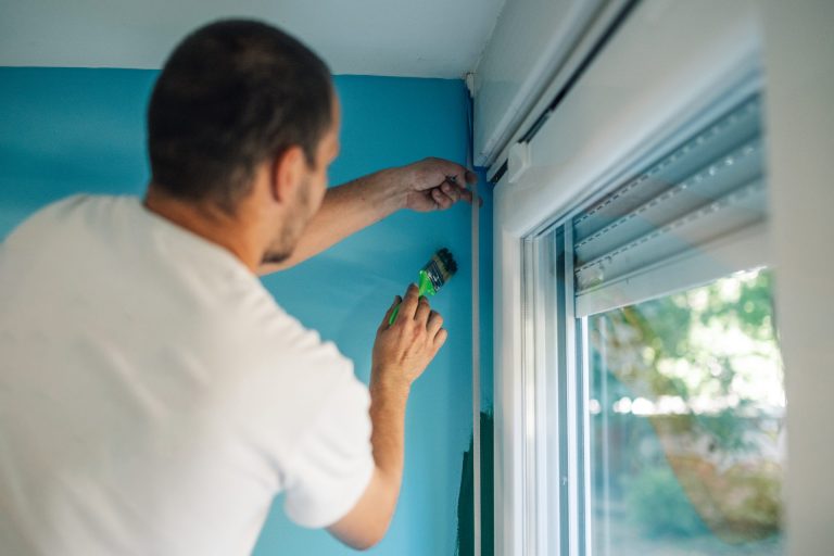Man painting blue wall near window frame